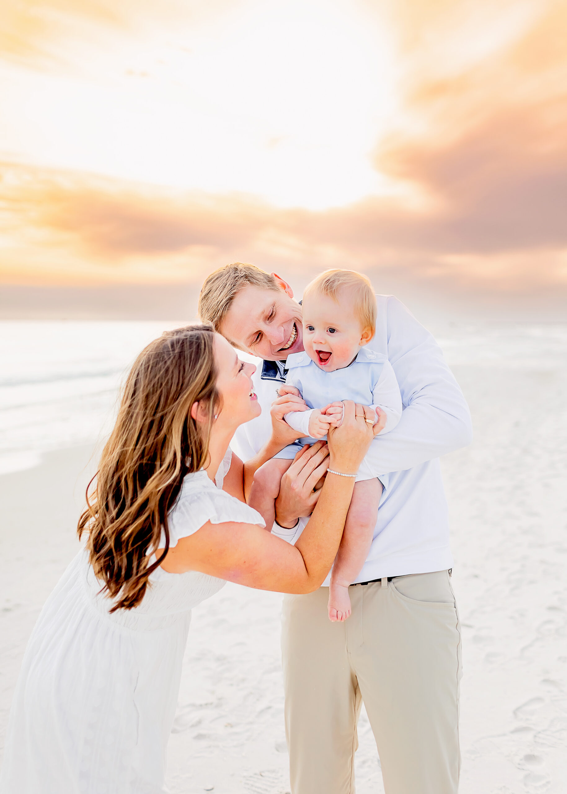 parents snuggle their baby on the beach at gulf shores while photographer captures the sweet moment