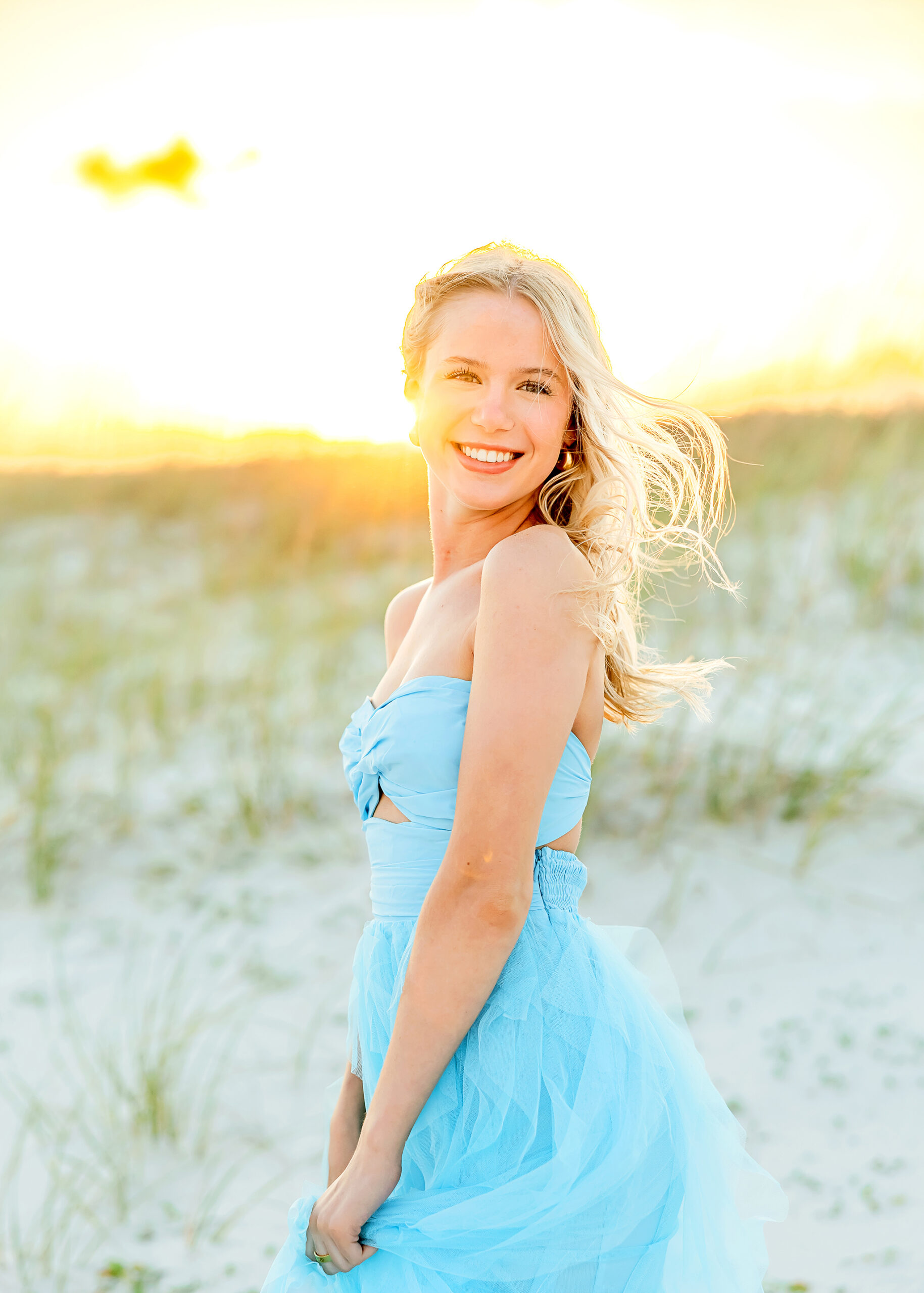 Senior poses on the beach by the dunes for photographer in Orange Beach